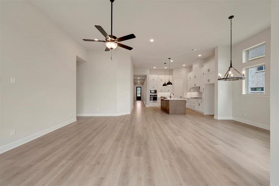 Unfurnished living room with suspended lighting, light wood-style flooring, and ceiling fan