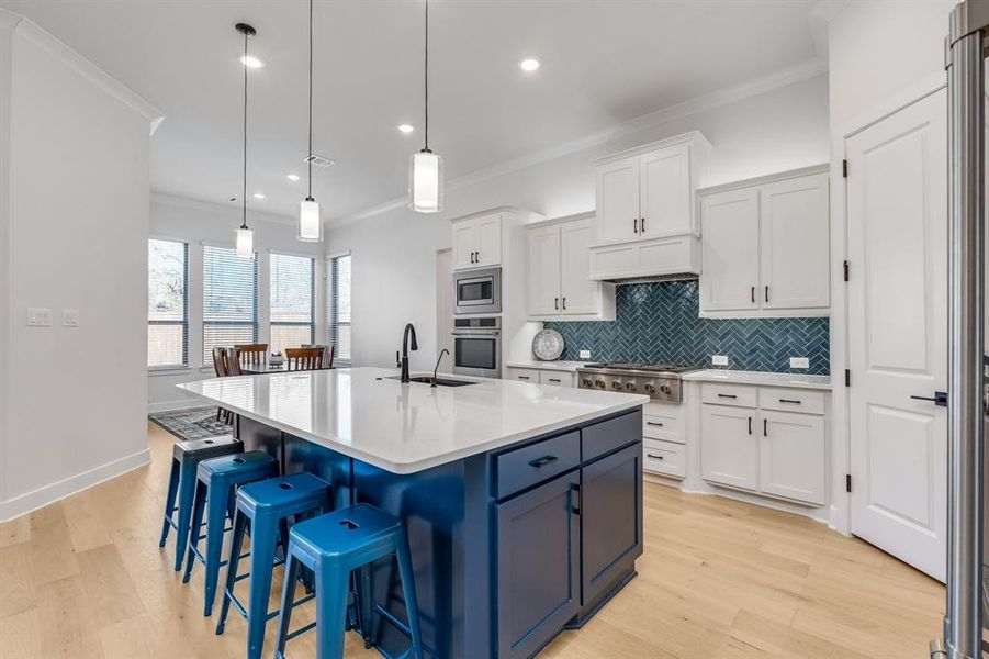 Kitchen with a center island with sink, crown molding, appliances with stainless steel finishes, decorative light fixtures, and white cabinetry