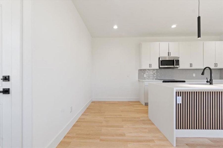 Kitchen featuring light countertops, stainless steel microwave, backsplash, light wood-style floors, and a sink