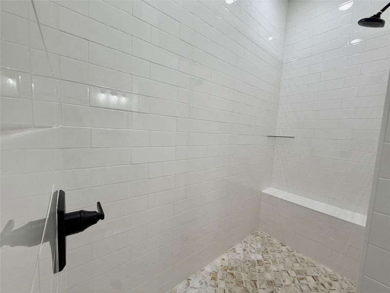 Shower enclosure featuring white subway tile walls, a built-in bench, a mosaic tile floor, and matte black fixtures
