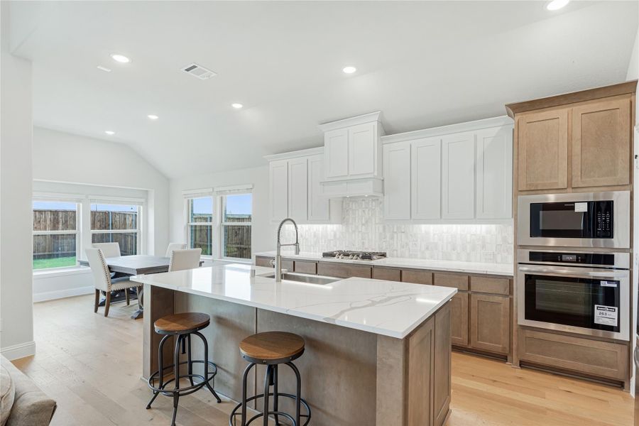Kitchen with large island, quartz countertops, white and wood cabinets, stainless steel appliances, and hardwood floors