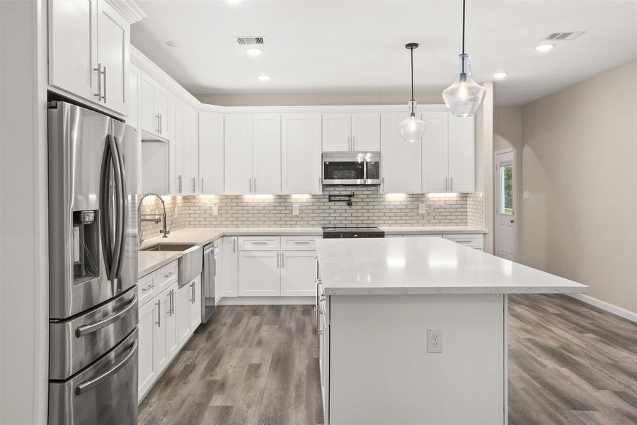Beautiful kitchen with quartz countertops, tile backsplash, under cabinet lighting, and stainless steel appliances