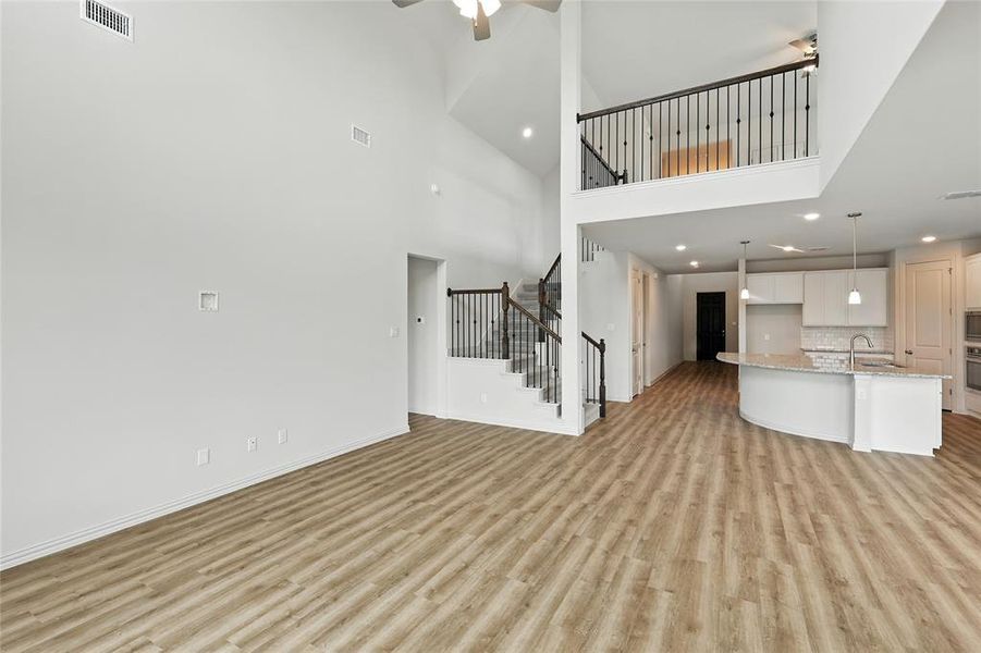 Unfurnished living room featuring a towering ceiling, light wood finished floors, ceiling fan, recessed lighting, and stairs Unfurnished living room featuring a towering ceiling, light wood finished floors, ceiling fan, recessed lighting, and stairs
