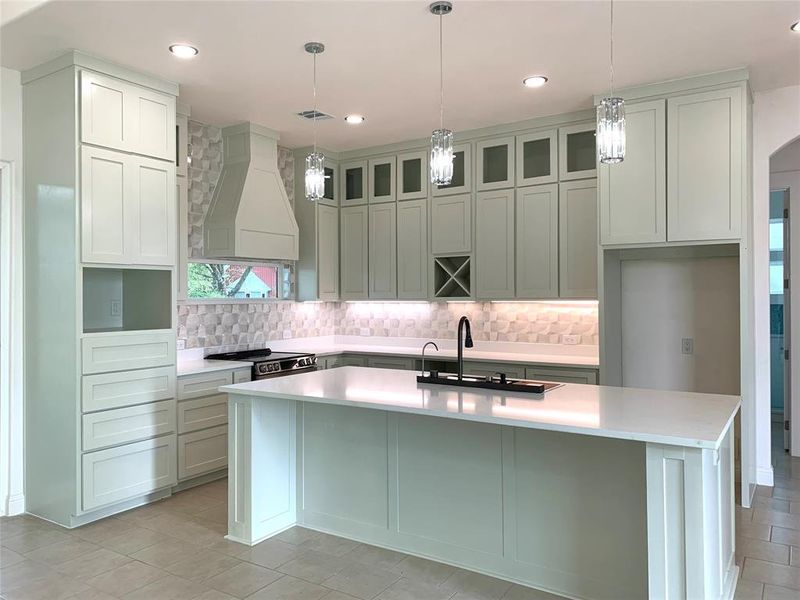 Kitchen featuring pendant lighting, a kitchen island with sink, decorative backsplash, glass insert cabinets, and recessed lighting Kitchen featuring pendant lighting, a kitchen island with sink, decorative backsplash, glass insert cabinets, and recessed lighting