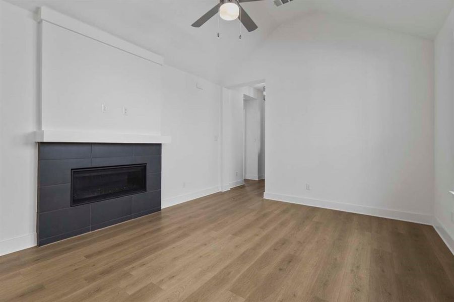 Unfurnished living room with a fireplace, wood finished floors, lofted ceiling, and a ceiling fan Unfurnished living room with a fireplace, wood finished floors, lofted ceiling, and a ceiling fan