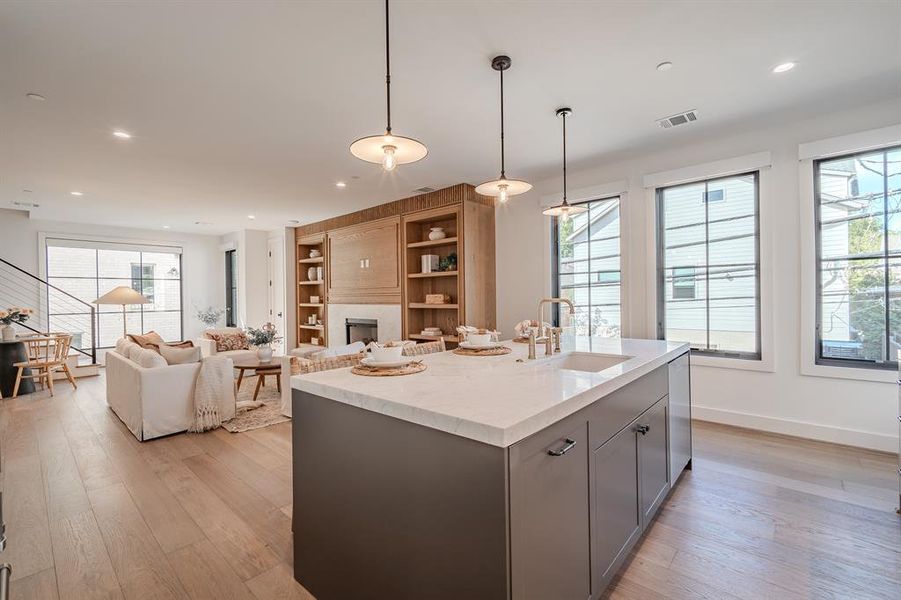 Kitchen with pendant lighting, gray cabinetry, a large fireplace, light stone counters, and light wood-style flooring