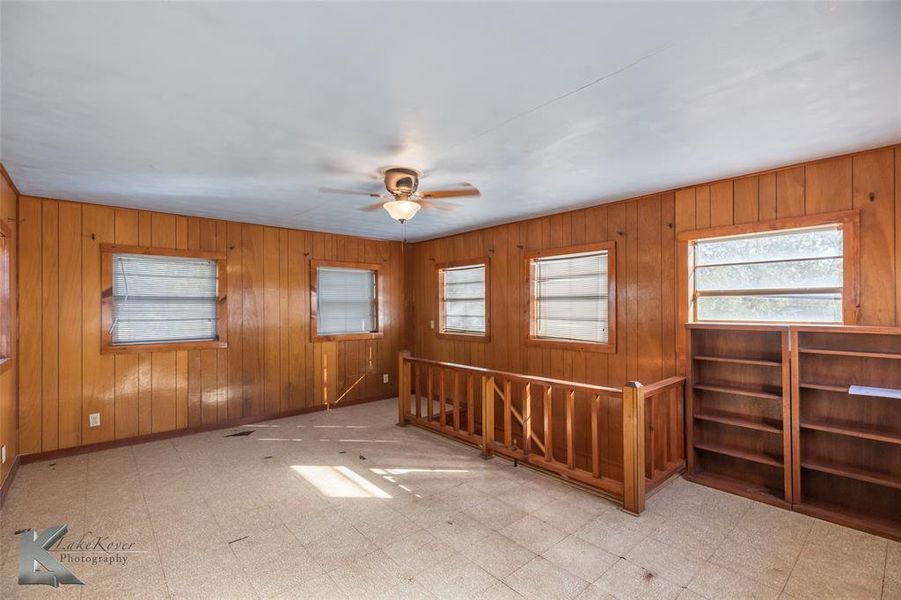 Empty room featuring light floors, wood walls, and ceiling fan Empty room featuring light floors, wood walls, and ceiling fan