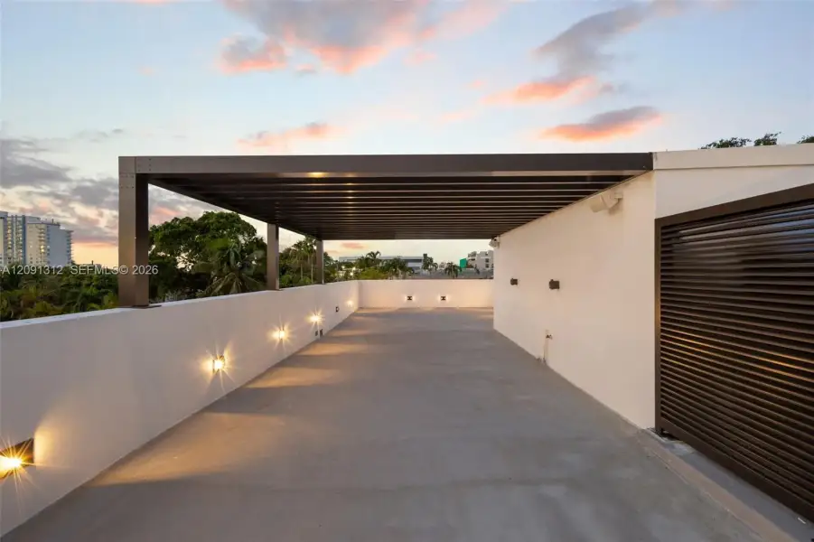 Rooftop terrace featuring a covered pergola, concrete flooring, smooth stucco parapet walls, and integrated wall-mounted lighting Rooftop terrace featuring a covered pergola, concrete flooring, smooth stucco parapet walls, and integrated wall-mounted lighting
