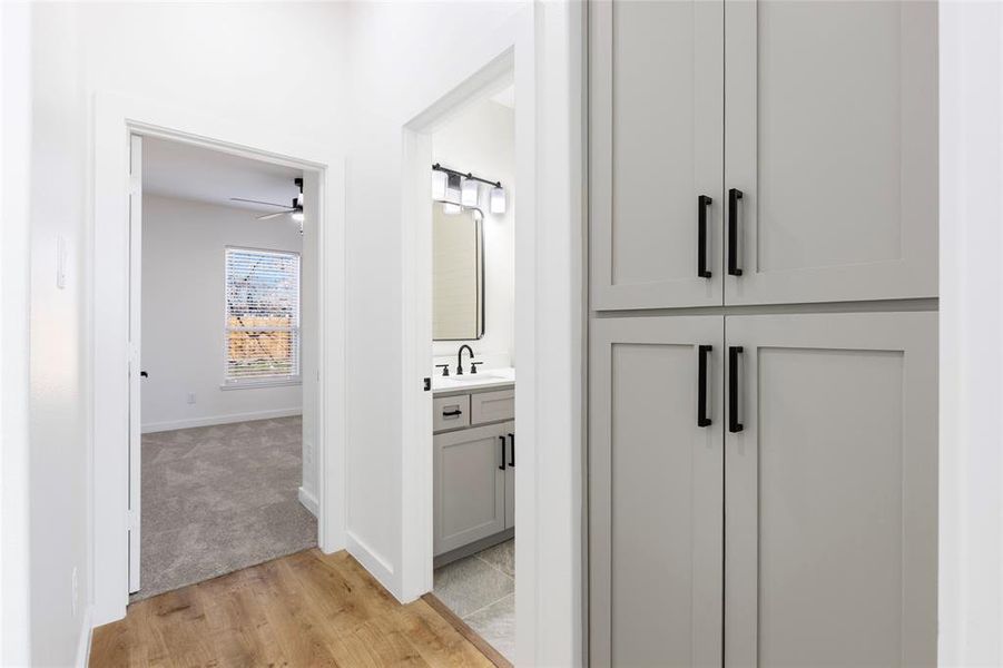 Corridor with light colored carpet, baseboards, light wood finished floors, and a sink