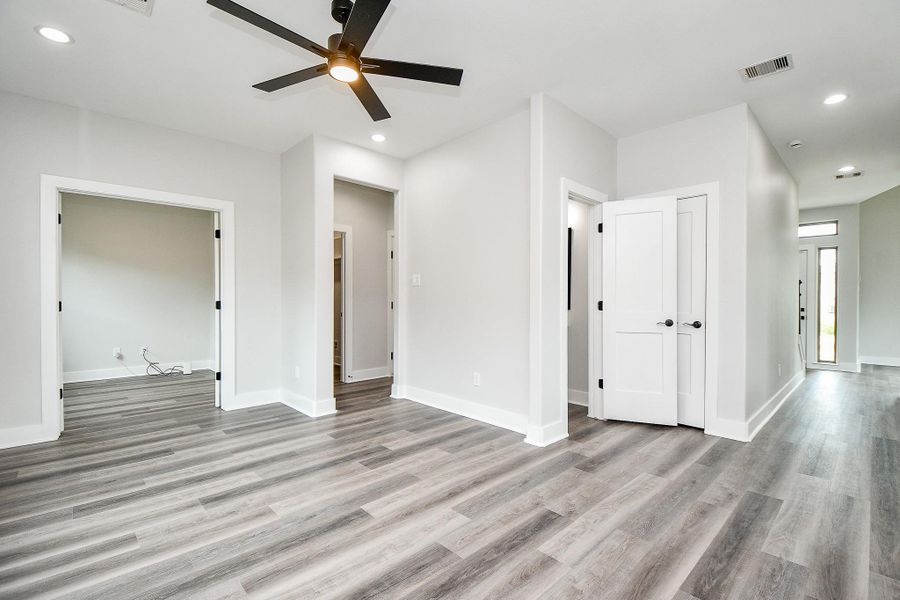 This is a view from kitchen of this bright, spacious family room with modern grey wood flooring, crisp white walls, and a contemporary black ceiling fan. The space features multiple doorways leading to adjacent study or office and a large under stairs closet for storage. The room benefits from recessed lighting and has a clean, airy feel. This is a view from kitchen of this bright, spacious family room with modern grey wood flooring, crisp white walls, and a contemporary black ceiling fan. The space features multiple doorways leading to adjacent study or office and a large under stairs closet for storage. The room benefits from recessed lighting and has a clean, airy feel.