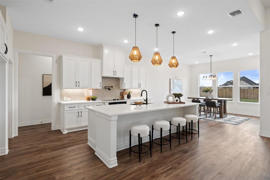 Kitchen featuring white cabinetry, tasteful backsplash, a kitchen bar, decorative light fixtures, and dark wood-type flooring Kitchen featuring white cabinetry, tasteful backsplash, a kitchen bar, decorative light fixtures, and dark wood-type flooring