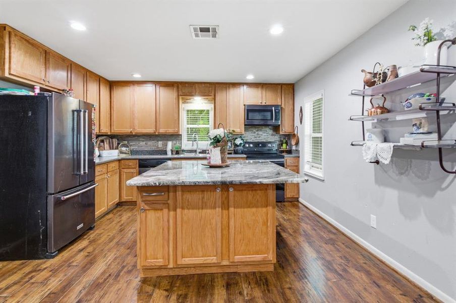 Open kitchen featuring an island with a stone-finish countertop, wood-finish flooring, wood cabinetry, recessed lighting, and a window with blinds