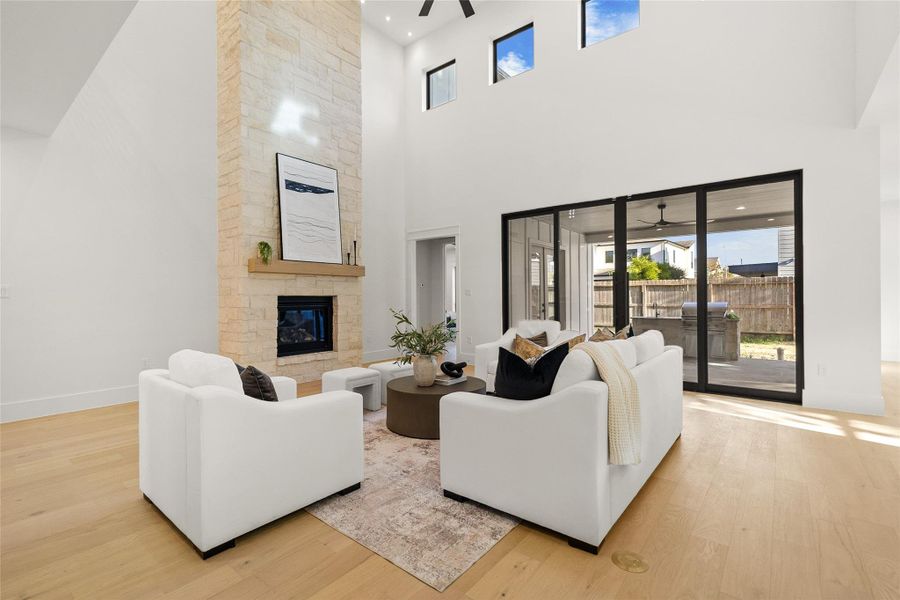 A floor-to-ceiling stone fireplace anchors this two-story living room, topped with a wood mantel and framed by stacked stone. Soaring ceilings and a row of clerestory windows bring in natural light, while sliding glass doors open to a covered outdoor living area with a built-in kitchen. Wide-plank hardwood floors and an open layout make this a comfortable space for gathering and relaxing.