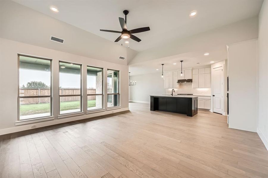 Unfurnished living room featuring vaulted ceiling, a sink, light wood finished floors, visible vents, and a ceiling fan Unfurnished living room featuring vaulted ceiling, a sink, light wood finished floors, visible vents, and a ceiling fan