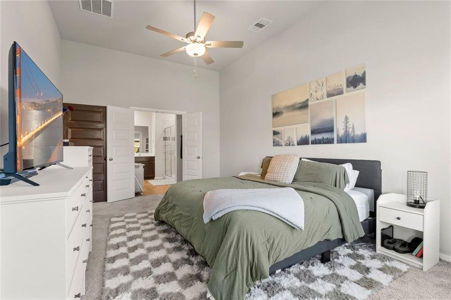 Primary bedroom downstairs featuring light-colored carpet, ensuite bathroom, a ceiling fan, and a towering ceiling
