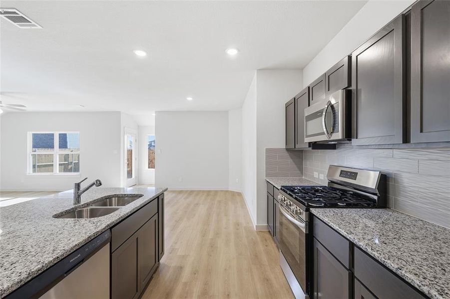Kitchen featuring stainless steel appliances, light stone countertops, light wood finished floors, open floor plan, and recessed lighting