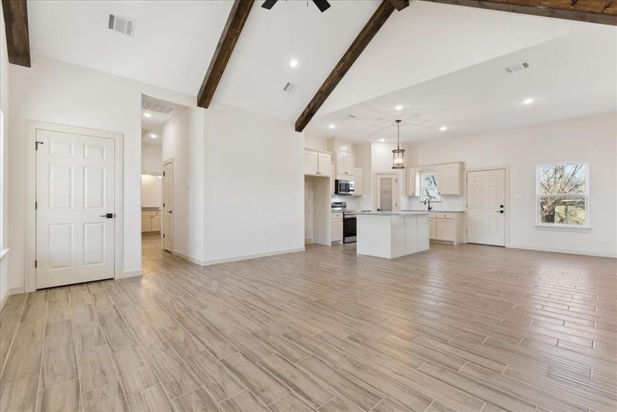 Unfurnished living room with beamed ceiling, ceiling fan, light wood-type flooring, and high vaulted ceiling