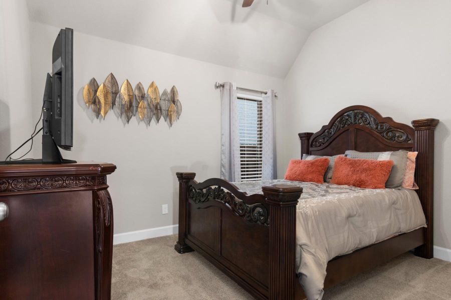 This cozy bedroom features neutral walls and carpeting create a warm atmosphere, complemented by a window with light curtains.