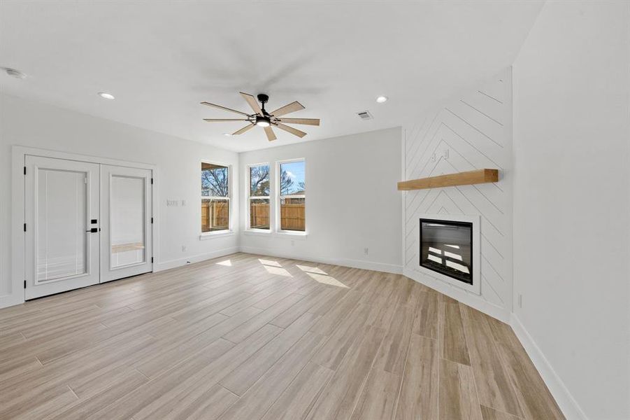 Unfurnished living room featuring a large fireplace, baseboards, light wood-style flooring, ceiling fan, and recessed lighting