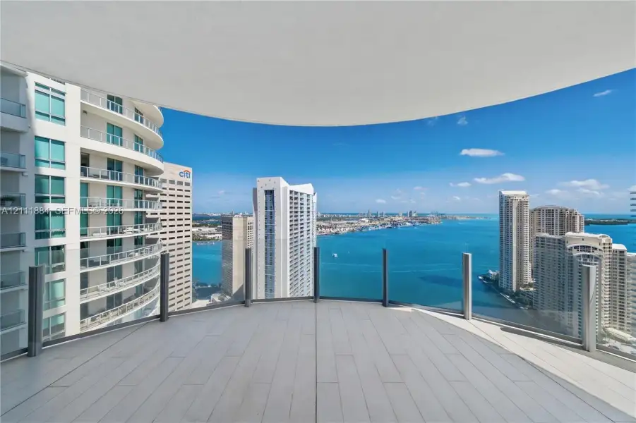 Curved expansive balcony featuring wood-finish flooring and floor-to-ceiling glass panel railings Curved expansive balcony featuring wood-finish flooring and floor-to-ceiling glass panel railings