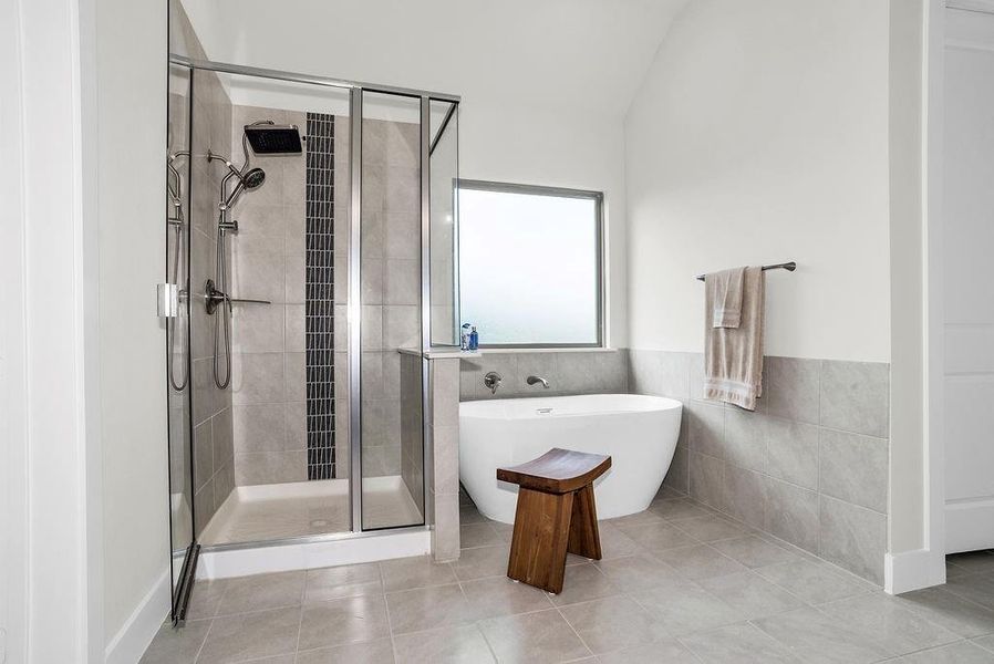 Main ensuite bath features dual vanity with wood-finish cabinetry, brush bronze faucets,  glass-enclosed steam shower with a tiled surround and vertical accent, a freestanding soaking tub ceramic tile floors and spacious walk-in closet with built-in shelving.