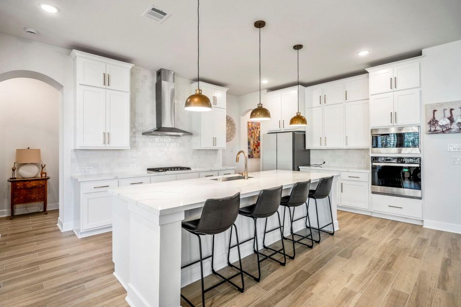 This modern kitchen features sleek white cabinetry, a large island with seating for four, stainless steel appliances, and stylish pendant lighting. The open layout and wood-look flooring create a welcoming feel.