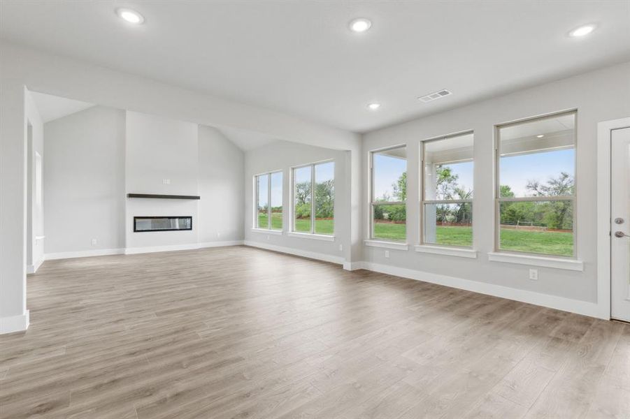 Unfurnished living room with light wood-style floors, a glass covered fireplace, lofted ceiling, and recessed lighting Unfurnished living room with light wood-style floors, a glass covered fireplace, lofted ceiling, and recessed lighting