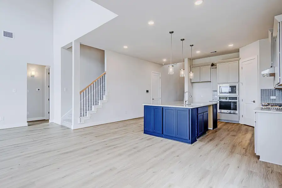 The kitchen stands out with a bold navy island, quartz countertops, and sleek pendant lighting. Soft cabinetry tones and stainless appliances create a polished, modern feel, while the adjacent staircase adds a stylish architectural detail. The kitchen stands out with a bold navy island, quartz countertops, and sleek pendant lighting. Soft cabinetry tones and stainless appliances create a polished, modern feel, while the adjacent staircase adds a stylish architectural detail.