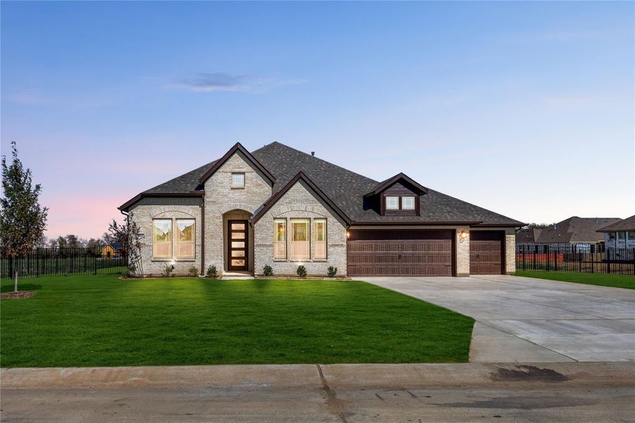 Single-story home with stone exterior, two-car garage, arched entry, and green front lawn at dusk