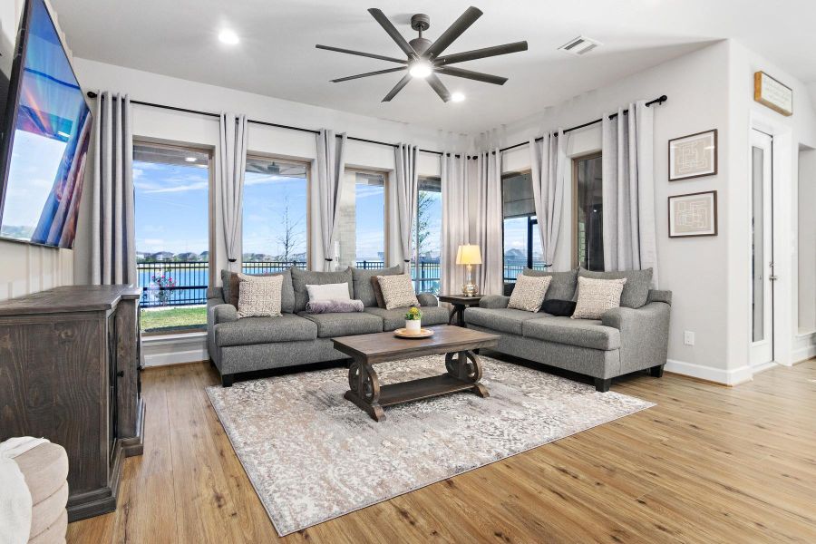 Bright and inviting living room with large windows offering a scenic view, featuring a stylish ceiling fan, with wall to ceiling windows. Perfect for relaxation and entertaining.