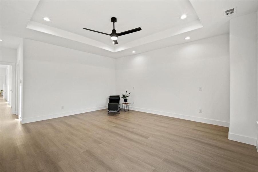 Empty room with a tray ceiling, light wood-type flooring, a ceiling fan, and recessed lighting