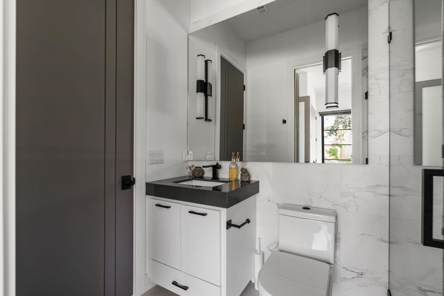 The ensuite bathroom continues the clean, modern feel with the floating style vanity, black countertop, matte black fixtures, a rectangular undermount sink, modern wall sconces, and a glass enclosed walk-in shower with marble style tile and built-in niches. Also accessible from the entertaining spaces.
