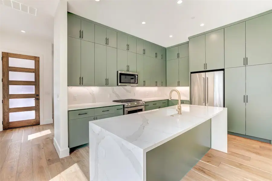 Kitchen featuring green cabinetry, high end appliances, recessed lighting, tasteful backsplash, and light wood-style floors