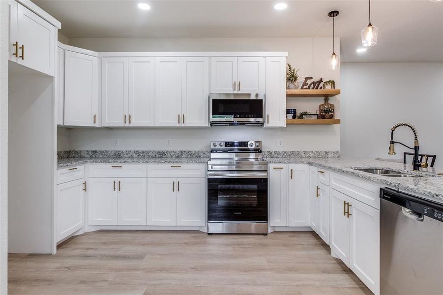 Kitchen featuring appliances with stainless steel finishes, sink, light wood-type flooring, light stone countertops, and white cabinetry