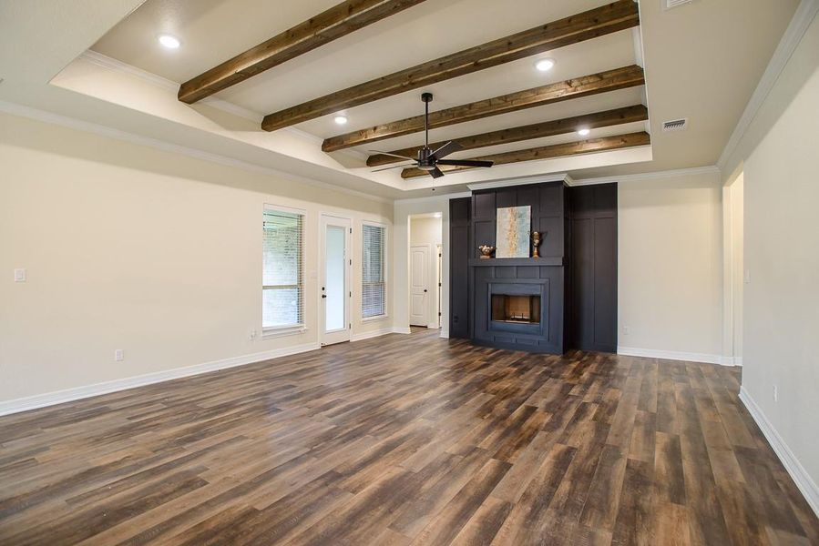 Unfurnished living room with a ceiling fan, dark wood finished floors, a fireplace, beamed ceiling, and crown molding Unfurnished living room with a ceiling fan, dark wood finished floors, a fireplace, beamed ceiling, and crown molding