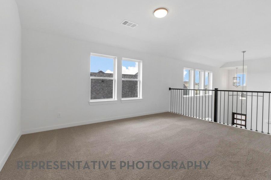 The game room features bright windows and decorative balusters overlooking the family room, creating an open, connected space for fun and entertainment.