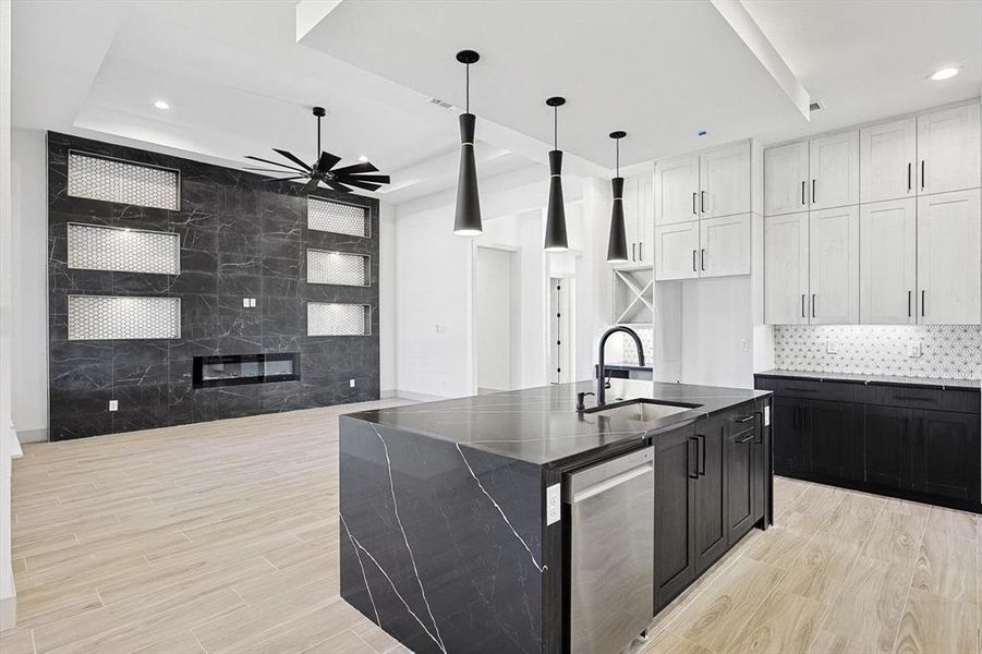 Kitchen featuring stainless steel dishwasher, a kitchen island with sink, sink, pendant lighting, and white cabinetry