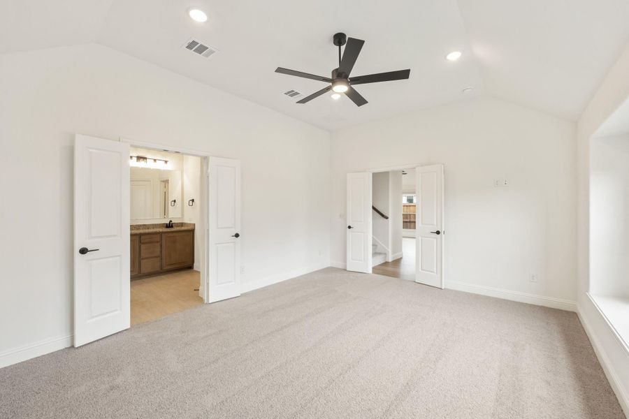 Empty master bedroom with carpet, ceiling fan, and open ensuite bathroom door Empty master bedroom with carpet, ceiling fan, and open ensuite bathroom door