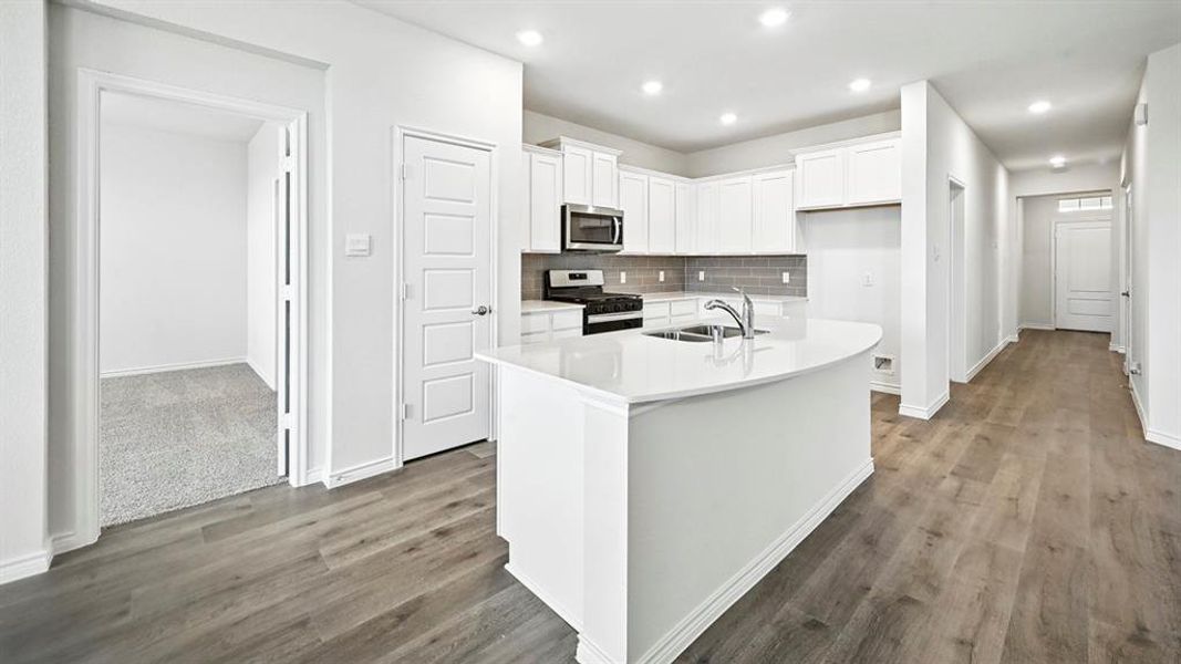 Modern kitchen featuring white cabinetry, stainless steel appliances, a center island with sink, and light-tone wood-finish flooring