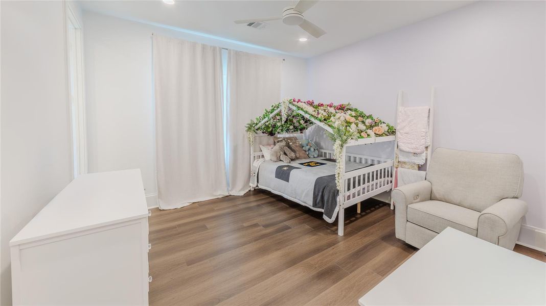 This cozy bedroom features a charming child's bed with a floral canopy, a comfortable armchair, and sleek hardwood flooring. The space is bright and airy, enhanced by soft lighting and neutral tones.