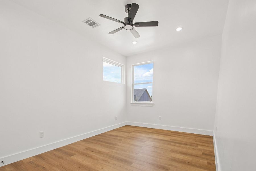 Crisp white walls pair with warm wood floors in a sunlit secondary bedroom. Crisp white walls pair with warm wood floors in a sunlit secondary bedroom.