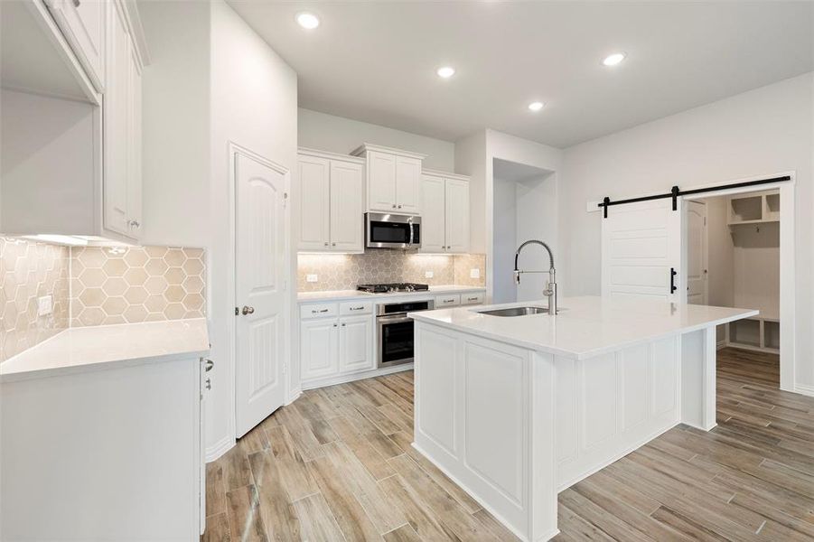 Kitchen with a barn door, white cabinets, a center island with sink, light stone countertops, and recessed lighting