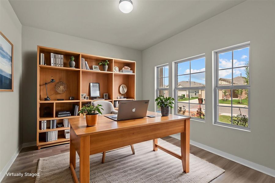 A well-lit home office features hardwood-style flooring and multiple windows, providing a neighborhood view.