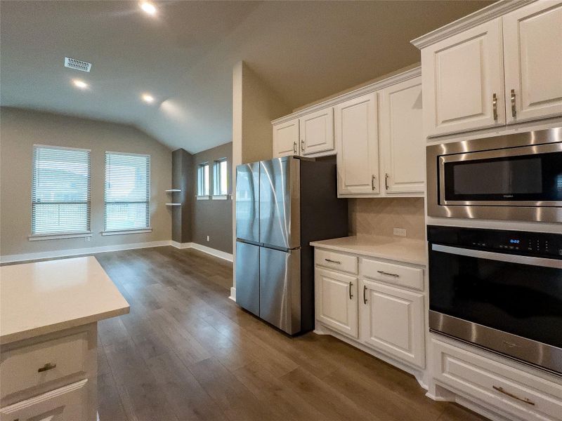 Kitchen featuring white cabinetry, appliances with stainless steel finishes, vaulted ceiling, recessed lighting, and dark wood-type flooring Kitchen featuring white cabinetry, appliances with stainless steel finishes, vaulted ceiling, recessed lighting, and dark wood-type flooring