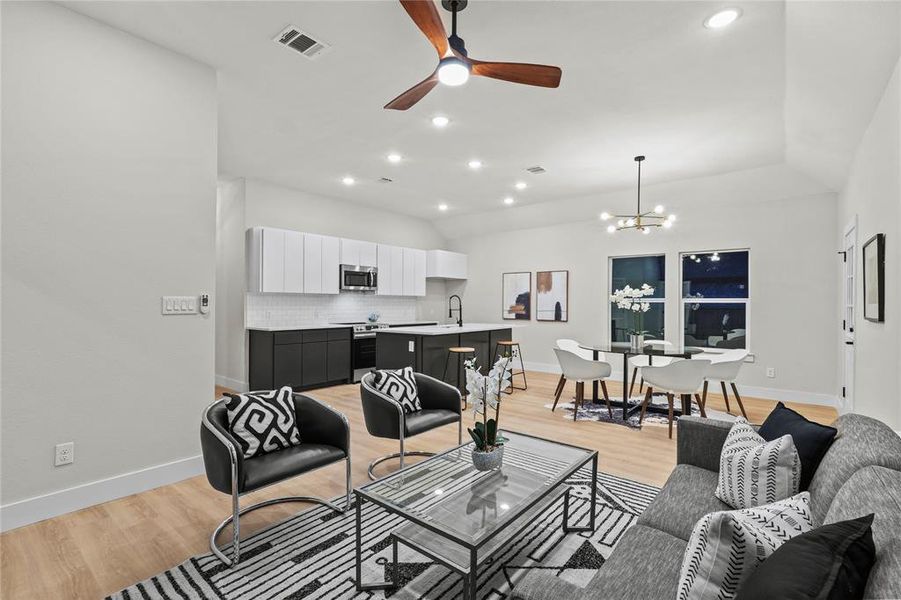 Living room with ceiling fan with notable chandelier, light hardwood / wood-style flooring, vaulted ceiling, and sink