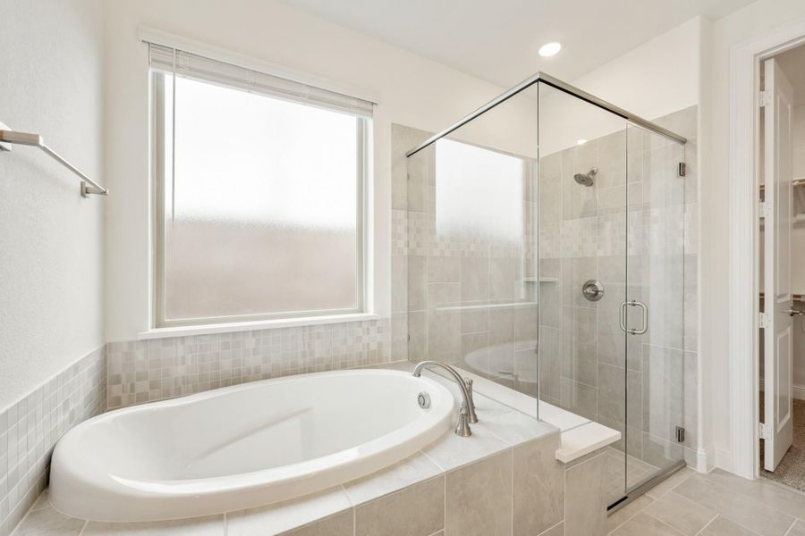 Master bathroom with oval soaking tub, glass-enclosed shower, and gray tile walls and floors