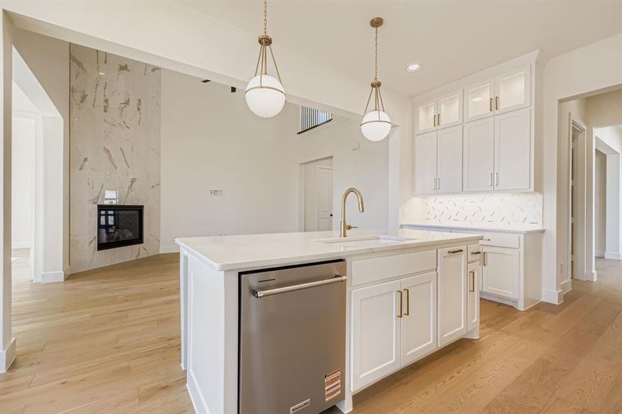 Kitchen with white cabinetry, pendant lighting, stainless steel dishwasher, light wood-type flooring, and light stone countertops