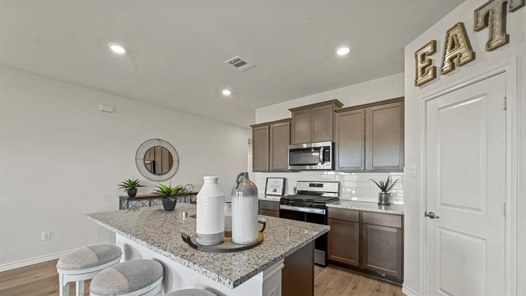 Kitchen featuring tasteful backsplash, light stone countertops, an island with sink, appliances with stainless steel finishes, and dark wood finished floors