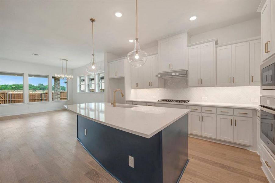 The kitchen features a spacious island with a white countertop and a dark base, pendant lighting, and white cabinetry with gold hardware
