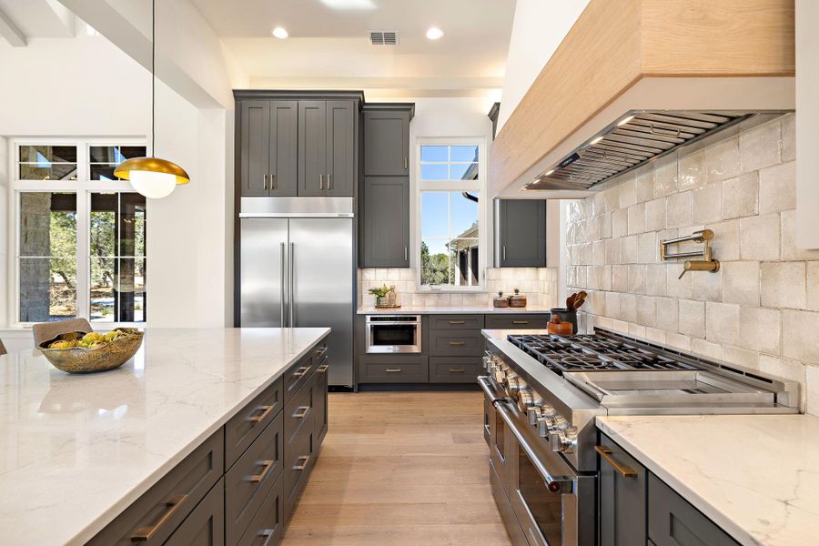 Kitchen with custom exhaust hood, high end appliances, tasteful backsplash, visible vents, and light wood-style floors